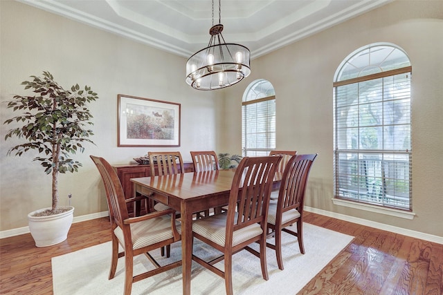 dining room with a notable chandelier, ornamental molding, a raised ceiling, and wood-type flooring