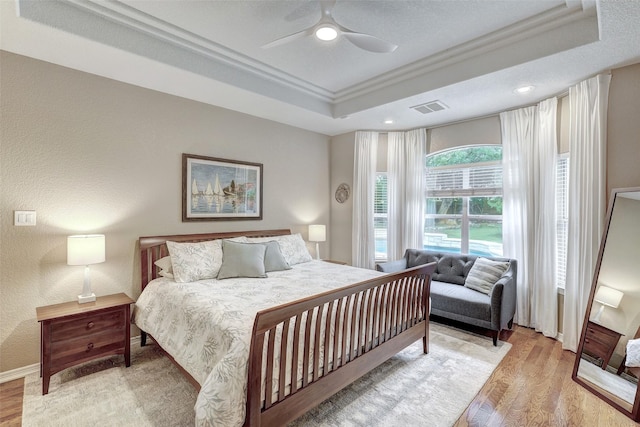 bedroom with light hardwood / wood-style floors, ceiling fan, a raised ceiling, and crown molding