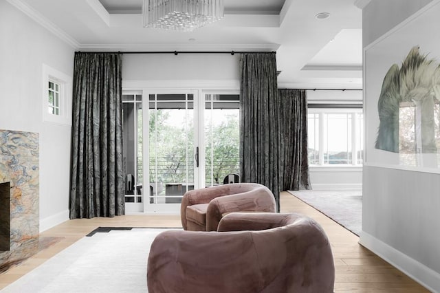 living area with a raised ceiling, a chandelier, ornamental molding, and light hardwood / wood-style floors