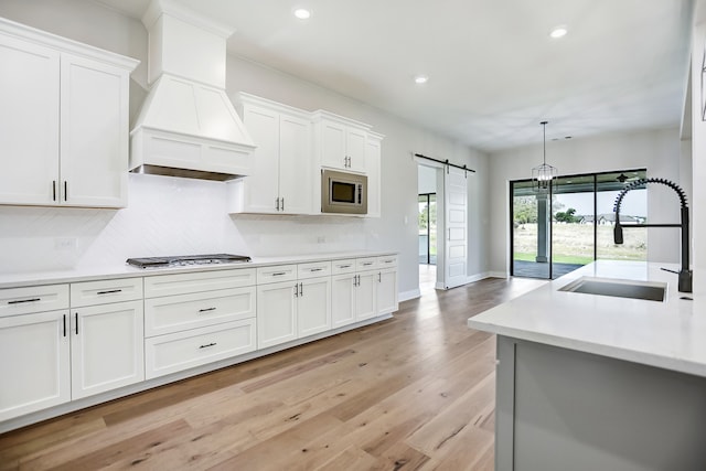 kitchen featuring stainless steel appliances, light wood-type flooring, a barn door, white cabinets, and sink