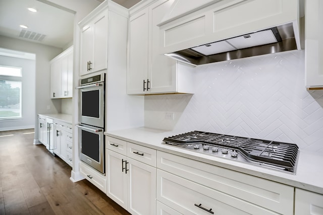 kitchen featuring appliances with stainless steel finishes, white cabinetry, tasteful backsplash, wall chimney range hood, and dark wood-type flooring