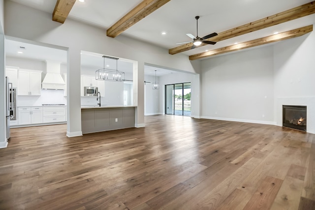 unfurnished living room with ceiling fan, beam ceiling, and light hardwood / wood-style flooring