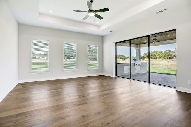 unfurnished room with a raised ceiling, ceiling fan, and dark hardwood / wood-style floors