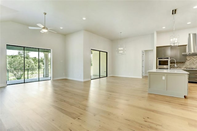 unfurnished living room with ceiling fan with notable chandelier, a towering ceiling, sink, and light hardwood / wood-style flooring