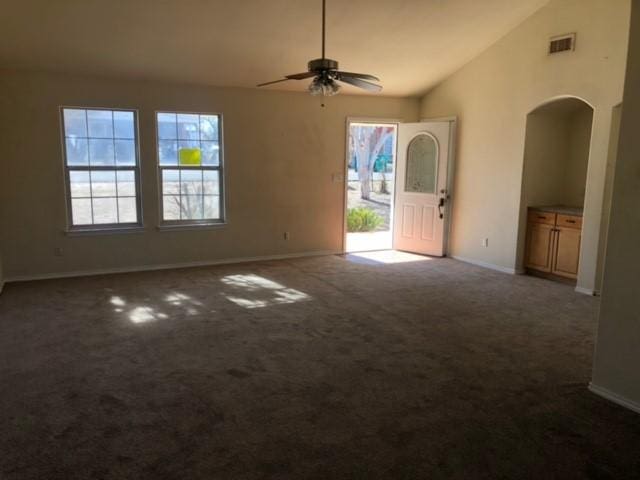 unfurnished room featuring dark carpet, ceiling fan, vaulted ceiling, and plenty of natural light