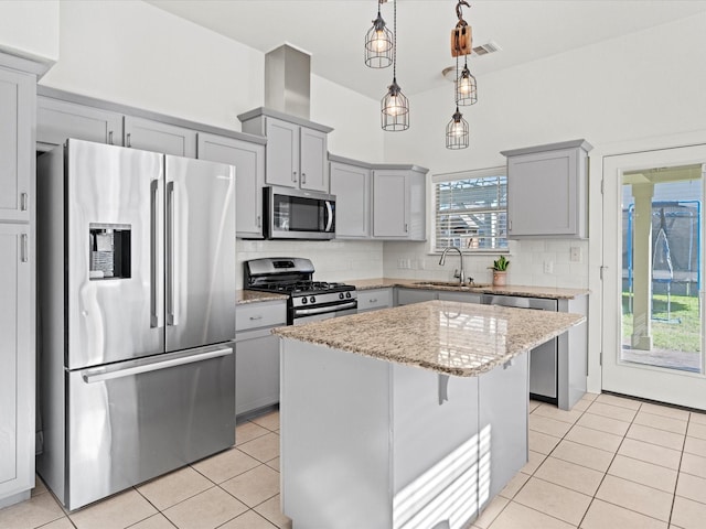 kitchen with appliances with stainless steel finishes, light stone countertops, a kitchen island, sink, and tasteful backsplash