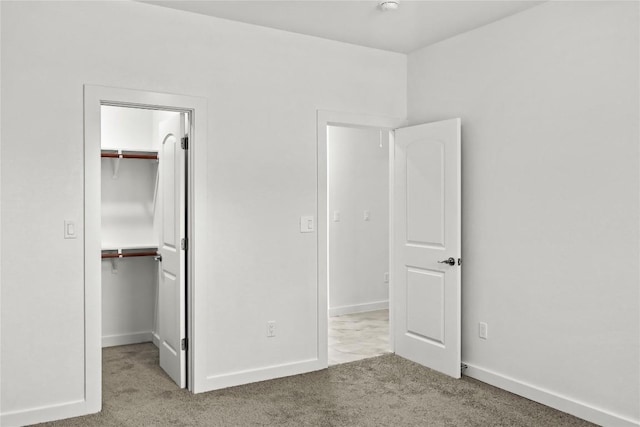 unfurnished bedroom with a spacious closet, carpet flooring, baseboards, and a closet