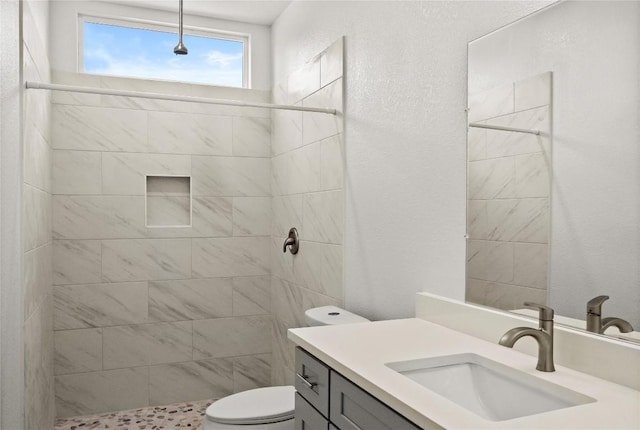 bathroom featuring vanity, toilet, a textured wall, and tiled shower