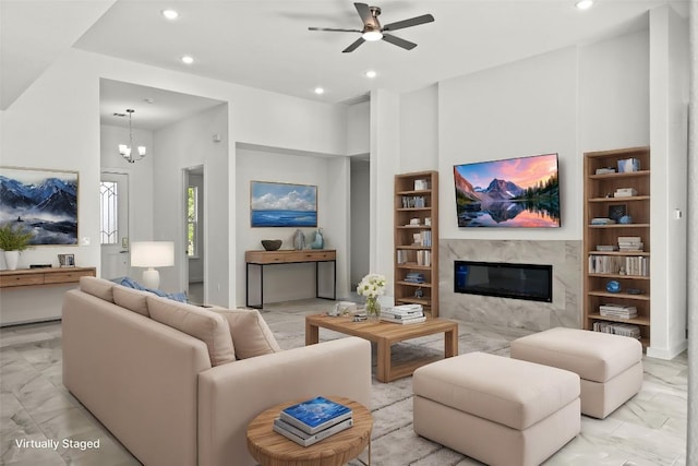 living room with built in shelves, marble finish floor, ceiling fan with notable chandelier, recessed lighting, and a premium fireplace