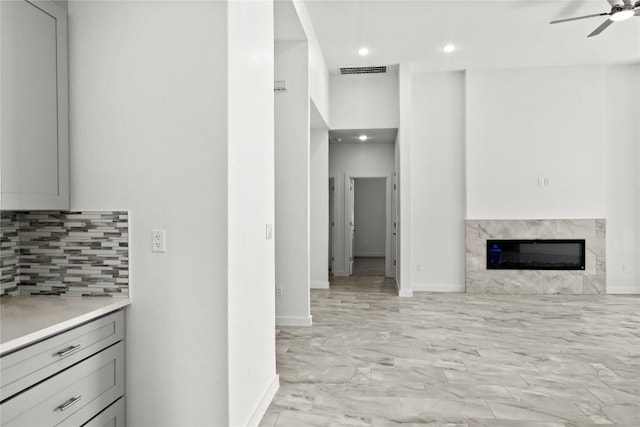 20714 Northland Dr, Lago Vista, TX 78645 - kitchen featuring gray cabinetry, light marble finish flooring, tasteful backsplash, a ceiling fan, and a high end fireplace