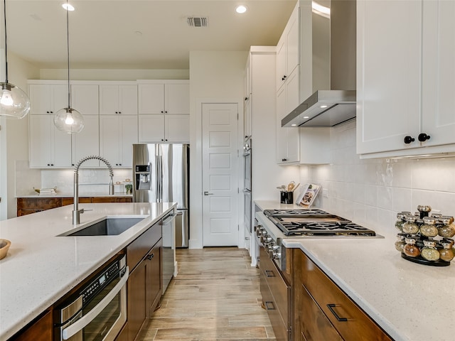 kitchen with light stone counters, decorative light fixtures, wall chimney range hood, white cabinetry, and sink