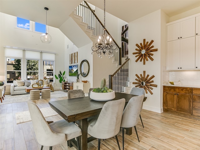 dining space featuring a towering ceiling, an inviting chandelier, and light wood-type flooring