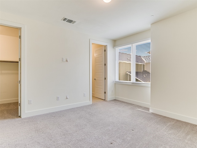 unfurnished bedroom featuring a walk in closet, a closet, and light carpet