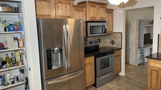 kitchen with dark stone countertops, appliances with stainless steel finishes, light tile patterned floors, ceiling fan, and tasteful backsplash