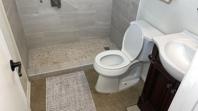 bathroom with toilet, a tile shower, and vanity