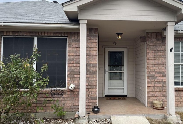 entrance to property featuring brick siding and a shingled roof