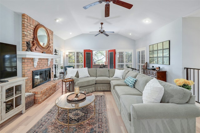 living room with a brick fireplace, ceiling fan, vaulted ceiling, and light hardwood / wood-style flooring