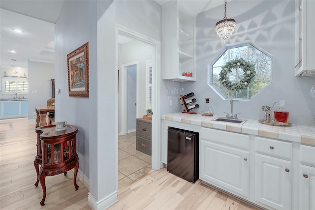 bar with tile countertops, refrigerator, white cabinets, decorative light fixtures, and sink