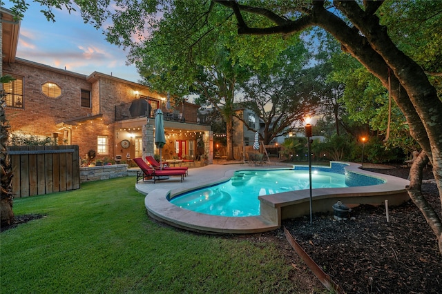 pool at dusk featuring a patio and a lawn