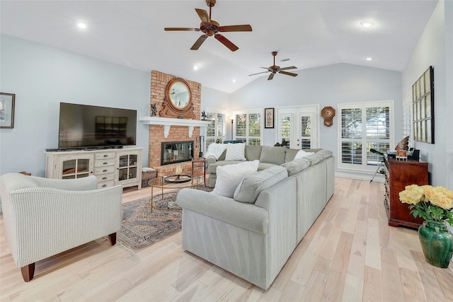 living room with vaulted ceiling, a brick fireplace, ceiling fan, and light hardwood / wood-style floors