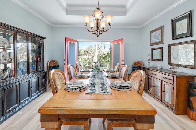 dining room featuring crown molding, light wood-type flooring, and a raised ceiling