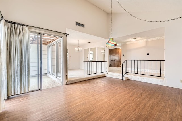 empty room featuring high vaulted ceiling, hardwood / wood-style flooring, a chandelier, and a wealth of natural light