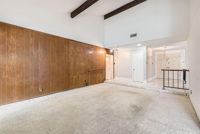 unfurnished room featuring beam ceiling, high vaulted ceiling, wooden walls, and light carpet