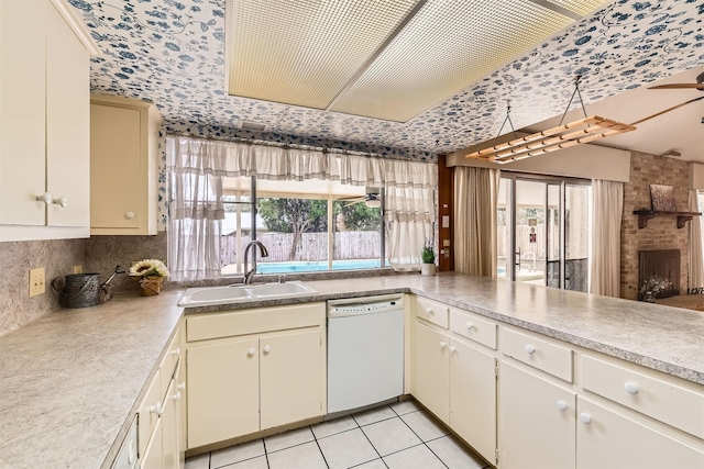 kitchen with sink, dishwasher, cream cabinets, light tile patterned floors, and a brick fireplace