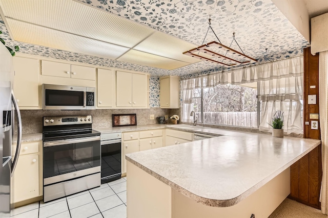 kitchen featuring cream cabinetry, appliances with stainless steel finishes, kitchen peninsula, light tile patterned floors, and sink