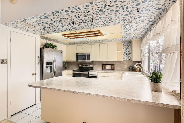 kitchen with kitchen peninsula, stainless steel appliances, cream cabinets, and sink