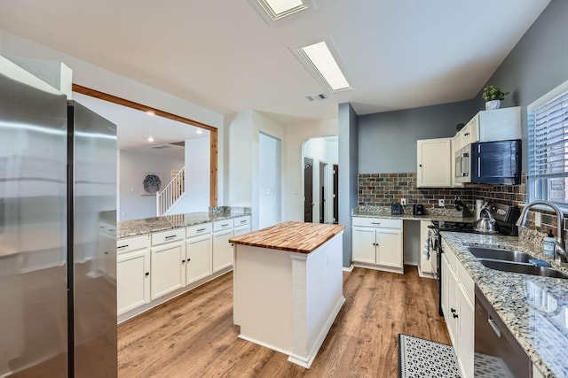 kitchen with stainless steel appliances, sink, white cabinetry, butcher block countertops, and decorative backsplash