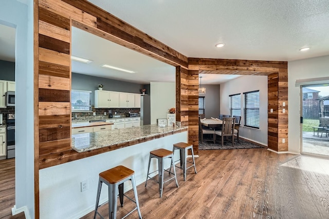 kitchen featuring light stone counters, kitchen peninsula, decorative backsplash, beam ceiling, and white cabinets