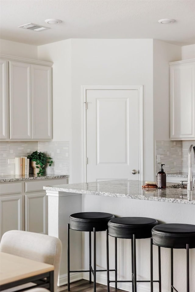 kitchen with light stone counters, hardwood / wood-style floors, tasteful backsplash, and white cabinetry