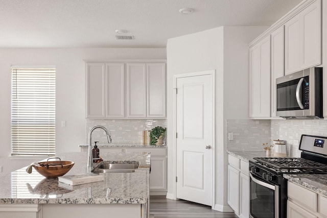 kitchen with a kitchen island with sink, appliances with stainless steel finishes, light stone counters, sink, and white cabinetry