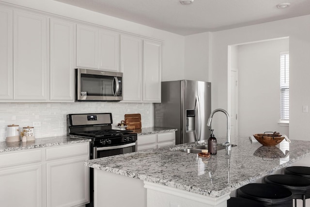 kitchen with appliances with stainless steel finishes, white cabinetry, a kitchen island with sink, and sink