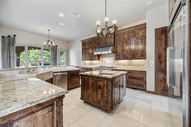 kitchen with extractor fan, refrigerator, pendant lighting, a center island with sink, and an inviting chandelier