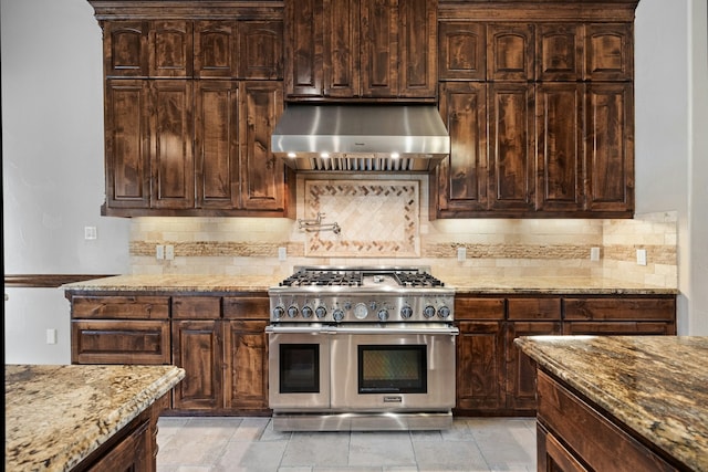 kitchen with range with two ovens, light stone counters, dark brown cabinets, range hood, and tasteful backsplash