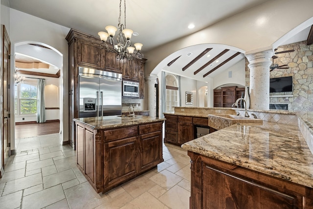 kitchen featuring a large island, hanging light fixtures, stone counters, built in appliances, and dark brown cabinets