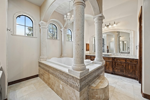 bathroom with decorative columns, an inviting chandelier, a relaxing tiled tub, and vanity