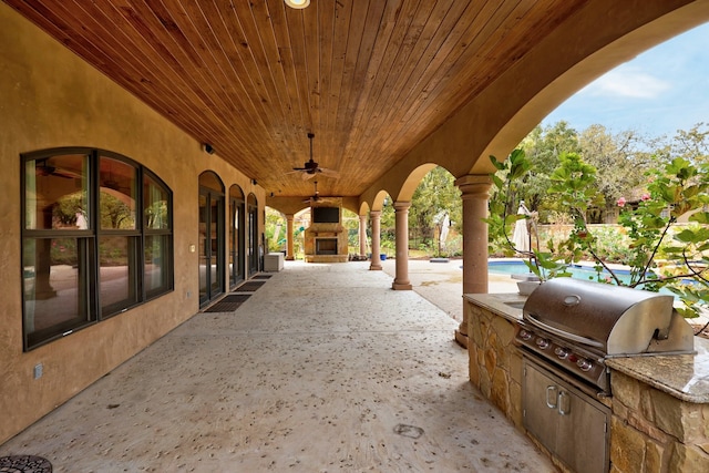 view of patio / terrace featuring exterior kitchen, a grill, ceiling fan, and an outdoor stone fireplace