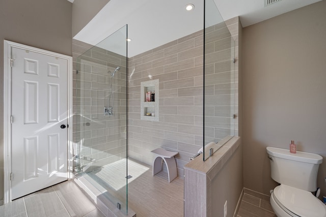 bathroom featuring toilet, tiled shower, and tile patterned floors