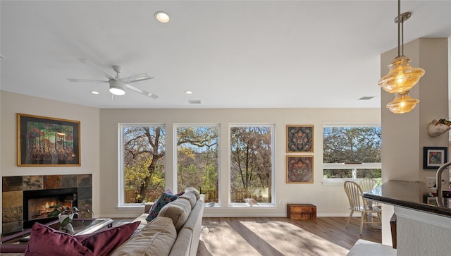 living room featuring wood-type flooring, a tiled fireplace, and ceiling fan