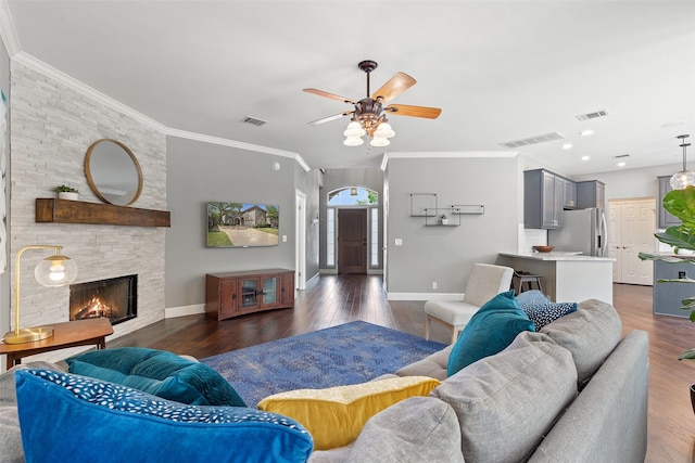 living room with dark wood-type flooring, ceiling fan, crown molding, and a stone fireplace