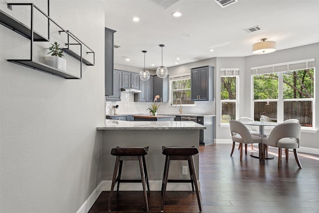 kitchen featuring kitchen peninsula, light stone countertops, pendant lighting, gray cabinets, and backsplash