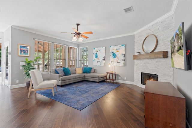 living room with ornamental molding, dark wood-type flooring, ceiling fan, and a stone fireplace