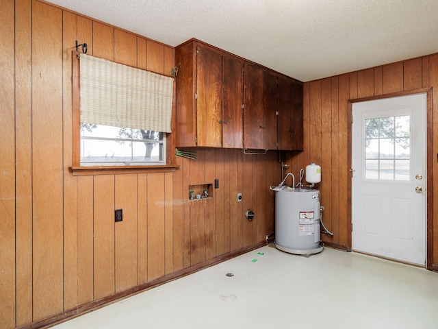 laundry area featuring a textured ceiling, wood walls, cabinets, electric water heater, and gas dryer hookup