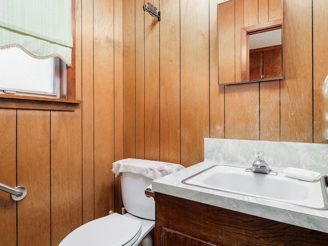 bathroom featuring toilet, wood walls, and vanity