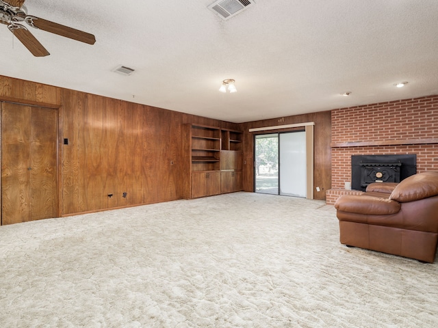 carpeted living room featuring a textured ceiling, ceiling fan, wooden walls, and a wood stove