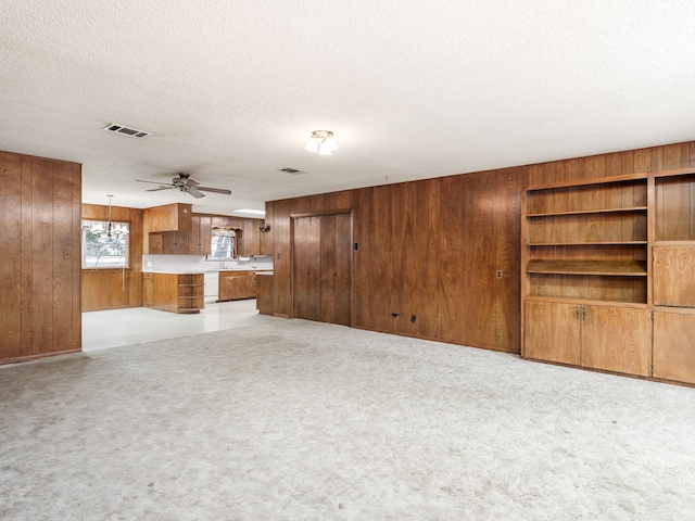 unfurnished living room with wood walls, a textured ceiling, light colored carpet, and ceiling fan