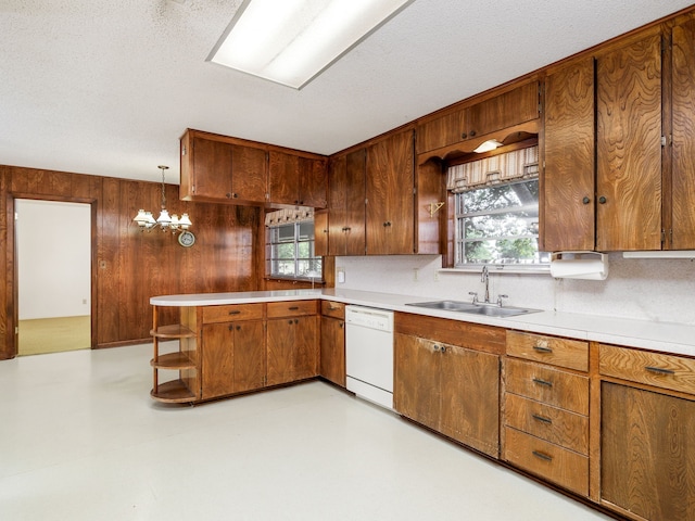 kitchen featuring dishwasher, a chandelier, decorative light fixtures, wooden walls, and sink